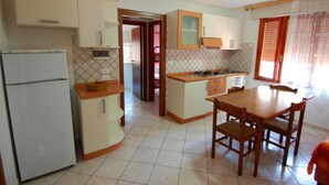 A compact kitchen with a refrigerator, a stove, and a dining table with chairs. - Comfortable apartment in lovely Rosolina Mare (Rosolina Mare)