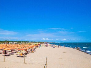 A beach with rows of sunbeds and umbrellas, a clear sky, and the ocean in the background. - Flat with shared garden 200 mt from the sea (Rosolina Mare)