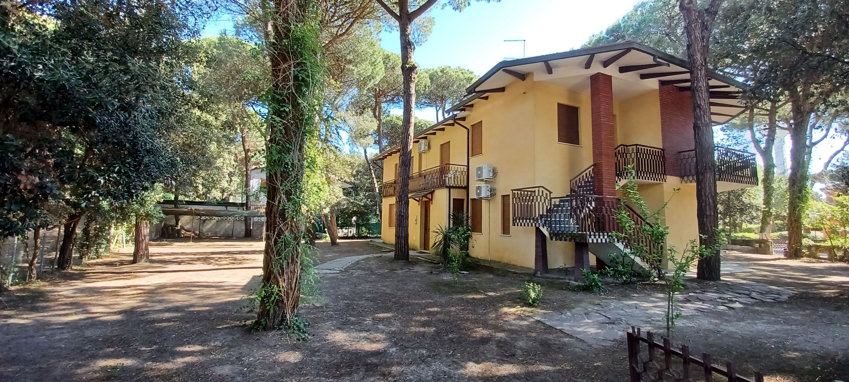 Un bâtiment jaune doté d’un balcon, entouré d’arbres et bordé d’un chemin en pierre.