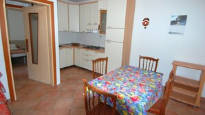 Een kleine keuken met witte kastjes, een eettafel met stoelen en een kleine koelkast.