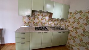 A kitchen with green cabinets, a gas stove, and a sink. - Accommodation with shared garden close to the sea (Rosolina Mare)
