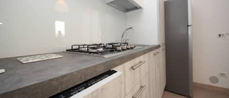 A modern kitchen with a stainless steel refrigerator, a built-in dishwasher, and a grey countertop.
