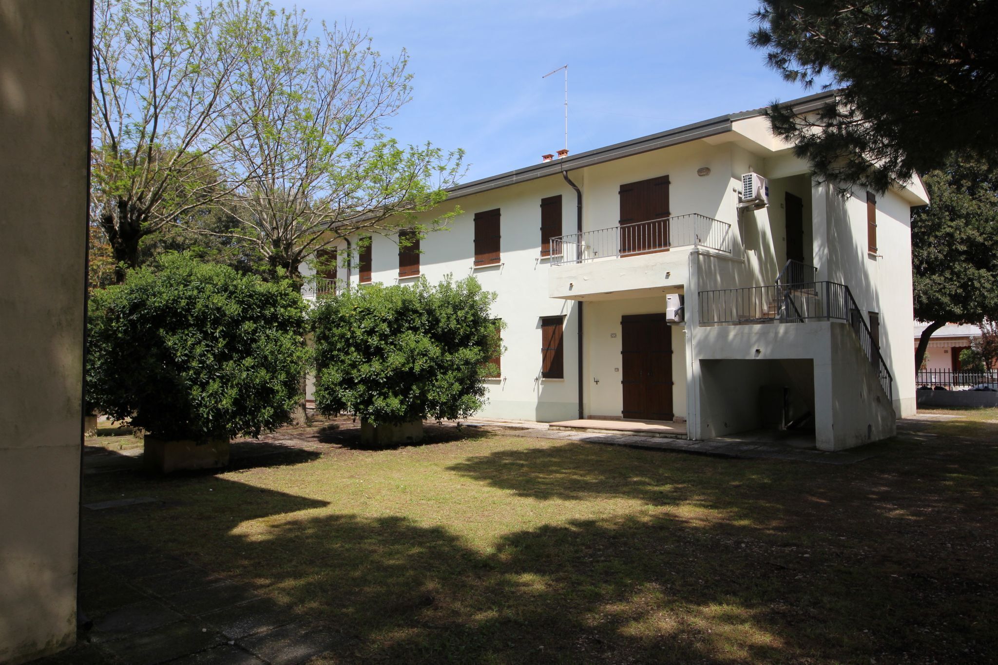 Un edificio a due piani con un balcone, un ingresso coperto e un piccolo giardino.