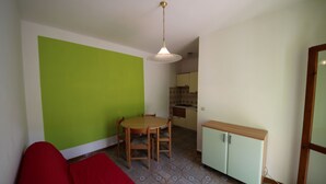 Ett kompakt bostadsutrymme med en matplats, ett litet kök och en röd soffa.