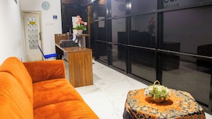 A hotel lobby with a reception desk, a sofa, a small table with a basket, and a large window with a sign reading "SAND'S".