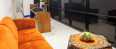 A hotel lobby with a reception desk, a sofa, a small table with a basket, and a large window with a sign reading "SAND'S".