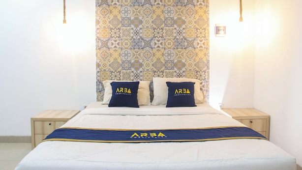 A hotel room with a patterned wallpaper, two bedside tables, a bed with a branded bedspread, and two pillows with the hotel logo.