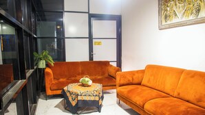 A room with a sofa, a small table with a patterned tablecloth, and a potted plant.