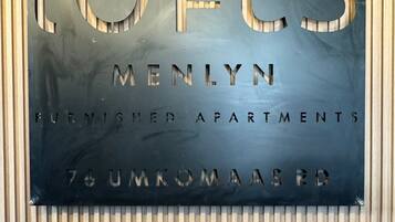 A sign for 'Lofts Menlyn Furnished Apartments' with a modern design and a view of the surrounding wooden paneling.