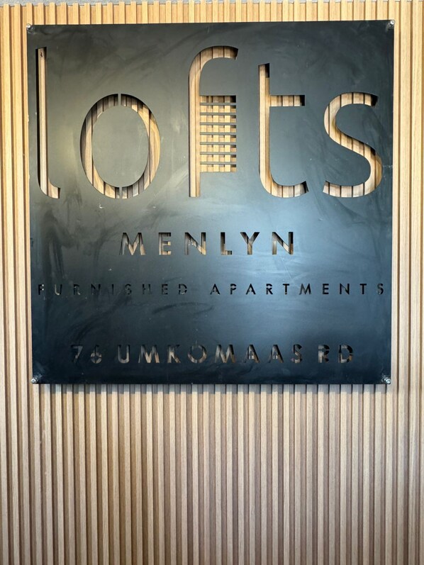 A sign for 'Lofts Menlyn Furnished Apartments' with a modern design and a view of the surrounding wooden paneling. - Menlyn Lofts (Pretoria)