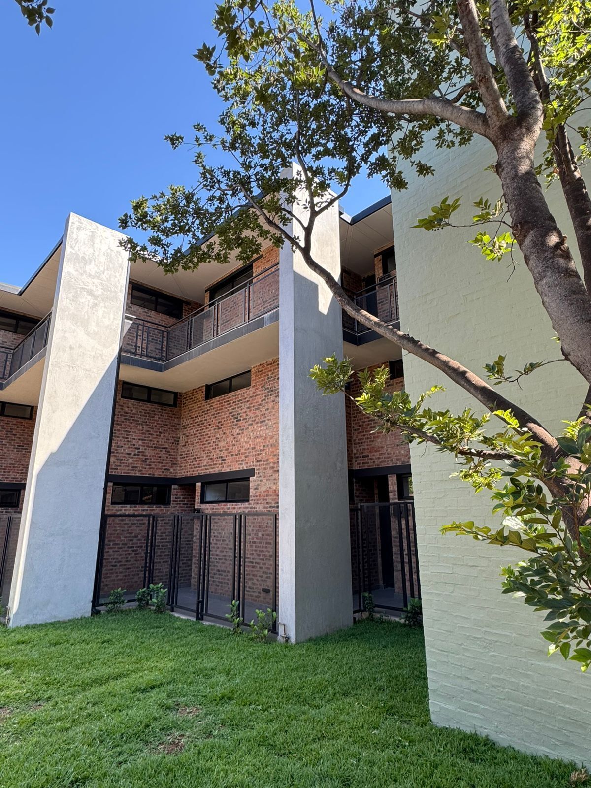 A modern multi-story building with brick and concrete exterior walls, large windows, and a grassy courtyard.