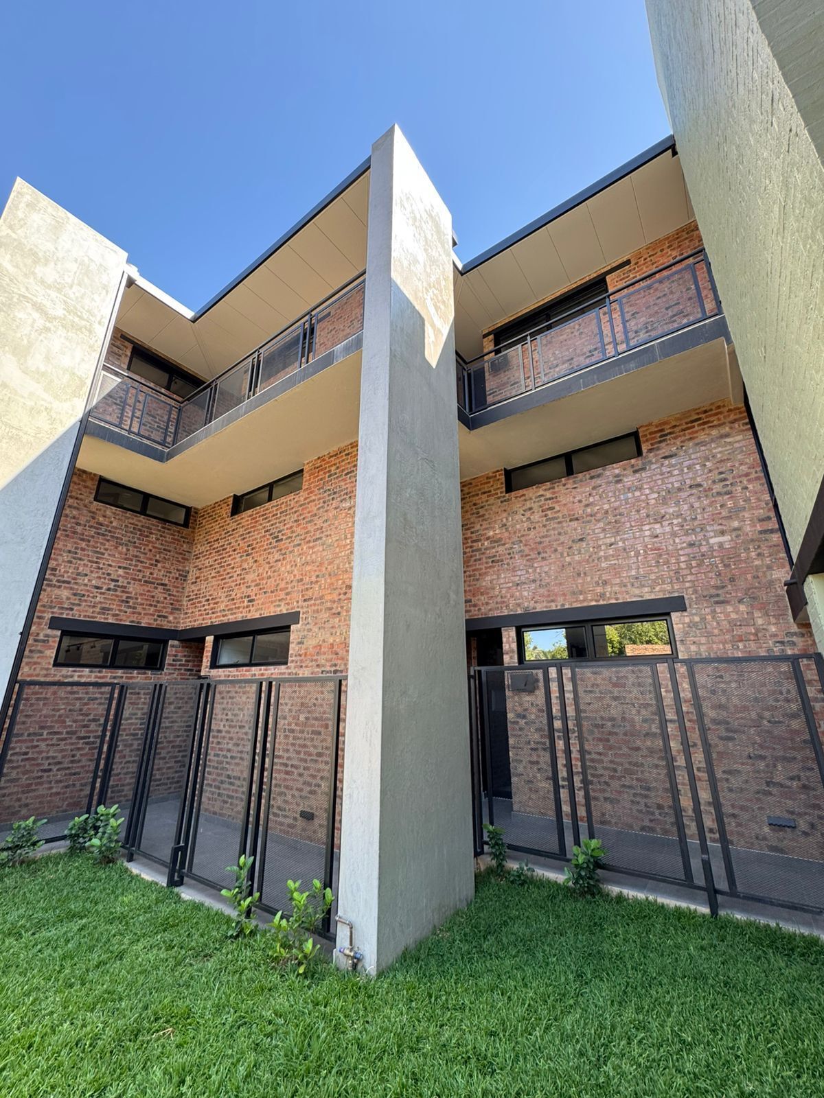 A modern multi-story building with brick facade, balconies, and a central concrete column.