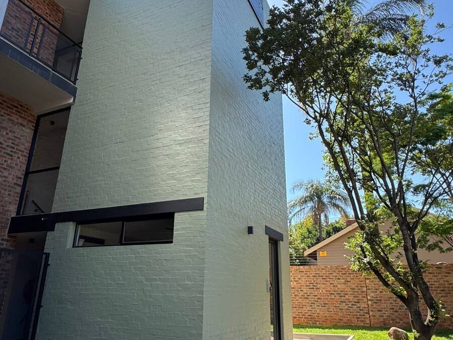 Um edifício moderno com fachada branca, uma porta visível e uma pequena árvore em primeiro plano.
