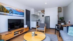 Un salon moderne avec un téléviseur, des meubles en bois, une table basse ronde et un tableau accroché au mur.