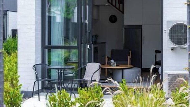 Une maison moderne dotée d’une porte vitrée donnant sur un coin repas avec une table et des chaises, un escalier et un appareil de climatisation visible.