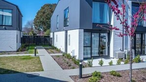 Un immeuble résidentiel moderne à deux étages, doté de grandes fenêtres, d’une pelouse bien entretenue et d’un petit arbre aux fleurs roses.
