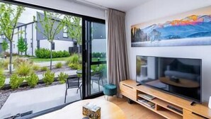 Un salon moderne avec un grand téléviseur, des portes-fenêtres coulissantes donnant sur un jardin et un tableau accroché au mur.