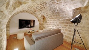A cozy, stone-walled room with a modern sofa, a flat-screen TV, and a floor lamp. - Chic apartment - 2BR/6P - Saint-Ambroise (Paris)