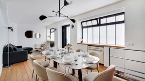 A modern dining area with a round table set for six, surrounded by beige chairs. A black ceiling light fixture is above the table. - Chic apartment - 2BR/6P - Saint-Ambroise (Paris)
