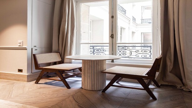 A room with a round table and two chairs, a window with curtains, and a view of a building with balconies. - Elegant apartment - 1BR/4P - Rue Saint-Honoré (Paris)