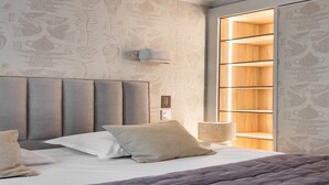 A modern bedroom with a tufted headboard, a large bed with a grey quilt, and a built-in wooden shelving unit with a soft light. - Elegant apartment - 1BR/4P - Rue Saint-Honoré (Paris)