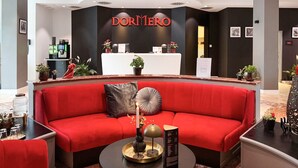 Una hall d'albergo moderna con un divano rosso, una reception e una macchina per il caffè.