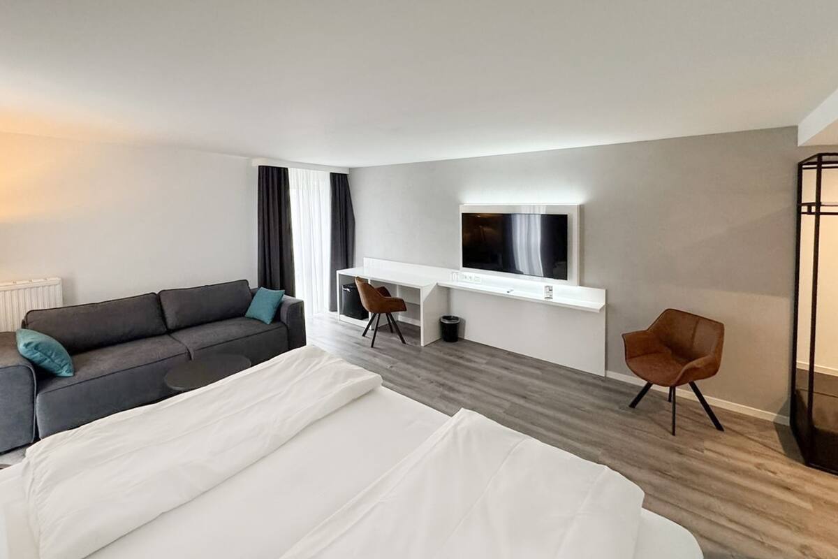 Una habitación de hotel moderna con una cama grande, un sofá, un escritorio con televisor y una silla.