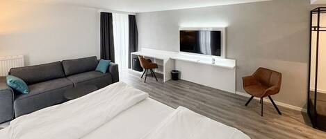 Une chambre d’hôtel moderne avec un grand lit, un canapé, un bureau avec une télévision et un fauteuil.