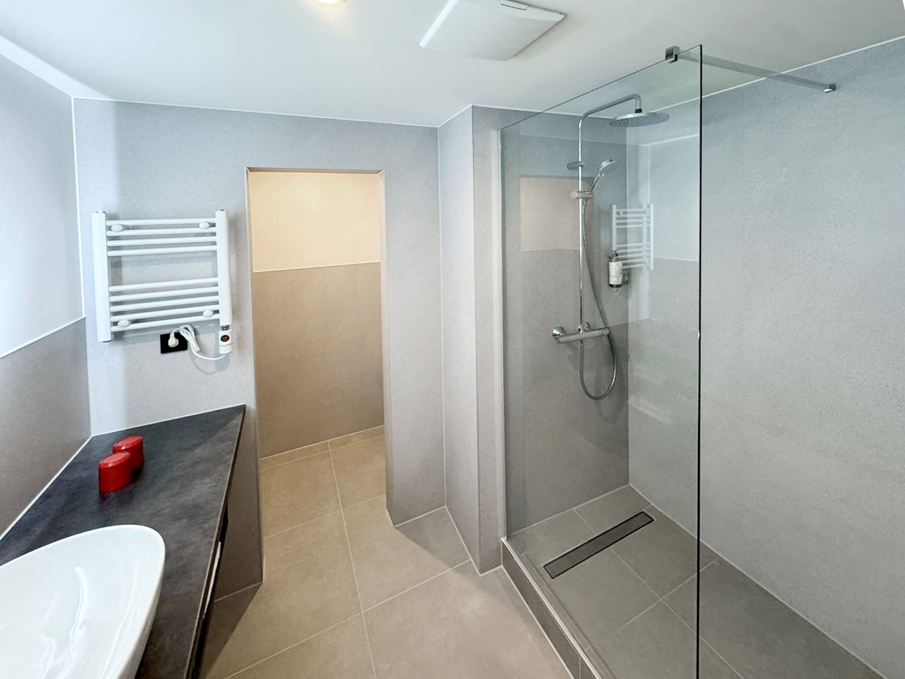 A modern bathroom with a glass shower enclosure, a white sink, and a towel rack.
