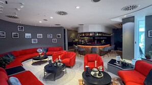 Una moderna area lounge con divani rossi, tavolini neri e un bancone bar.