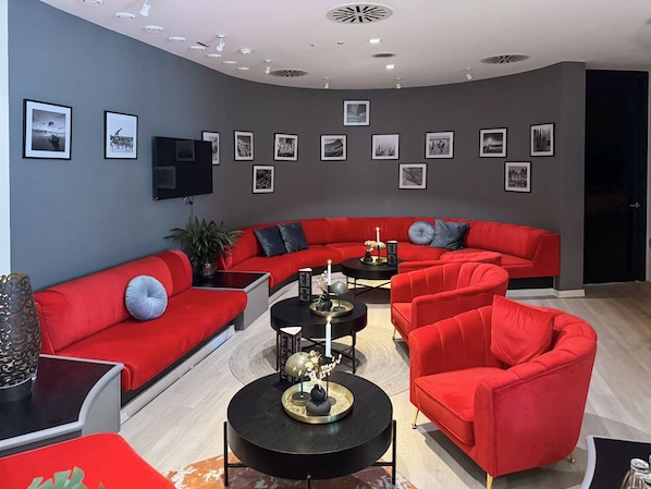 Een moderne woonkamer met rode banken, een zwarte salontafel en ingelijste foto's aan de muur.