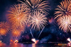 A nighttime view of fireworks over a body of water with a distant cityscape.