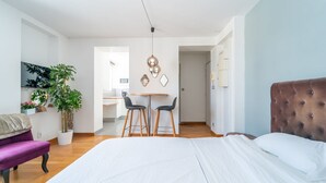 Una habitación de hotel moderna con una cama grande, una zona de comedor con dos sillas, una mesita y una planta en maceta.