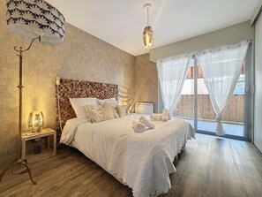 Une chambre avec un grand lit, une table de chevet, une lampe et une vue sur l’extérieur.