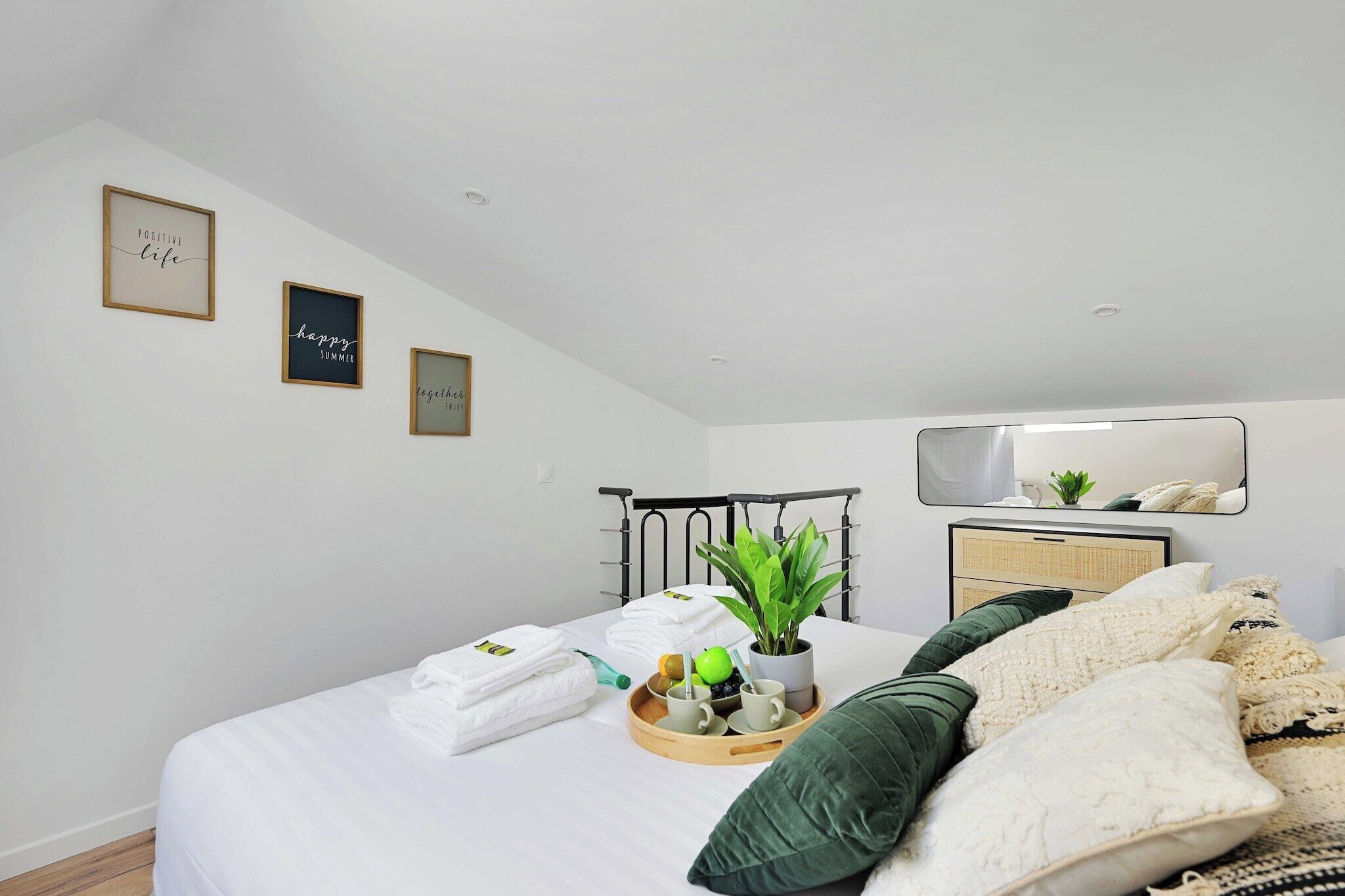 A neatly made bed with white linens, a tray with a plant, and a mirror above a dresser.