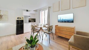 Un salon moderne comprenant un coin repas, une cuisine et un téléviseur fixé au mur.
