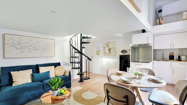 Un salon moderne avec un canapé bleu, une table à manger dressée pour quatre personnes et un escalier en colimaçon menant à un niveau supérieur.