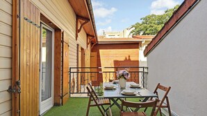 Une petite terrasse extérieure avec une table dressée pour deux personnes, entourée de chaises en bois, et une porte en bois avec une fenêtre.