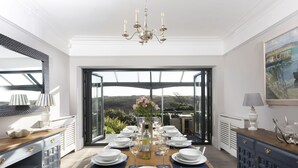 A dining area with a large table set for six, a chandelier, and a view of the outdoors. - Henscath House's characterful and spacious design perfectly caters for family and friends (Helston)