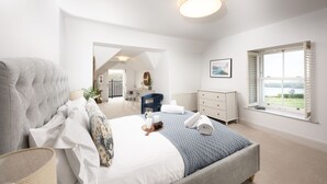 A spacious bedroom with a large bed, a dresser, a desk, and a window with a view. - Henscath House's characterful and spacious design perfectly caters for family and friends (Helston)