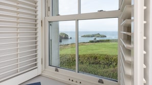 A room with a large window overlooking a grassy landscape and the sea. - Henscath House's characterful and spacious design perfectly caters for family and friends (Helston)