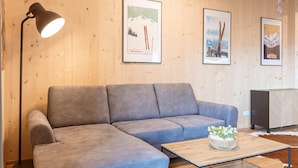Un salon moderne avec un canapé d’angle gris, un lampadaire, une table basse en bois agrémentée d’un arrangement floral et des tableaux encadrés accrochés au mur.