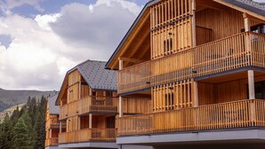A multi-story wooden building with balconies, set against a mountainous backdrop.