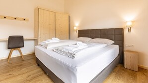 A neatly made bed with white linens and towels, a wooden wardrobe, a small bedside table, and a chair.