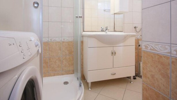 Une salle de bain équipée d’un lave-linge, d’une douche à parois de verre, d’un lavabo avec un miroir et d’un meuble de rangement.