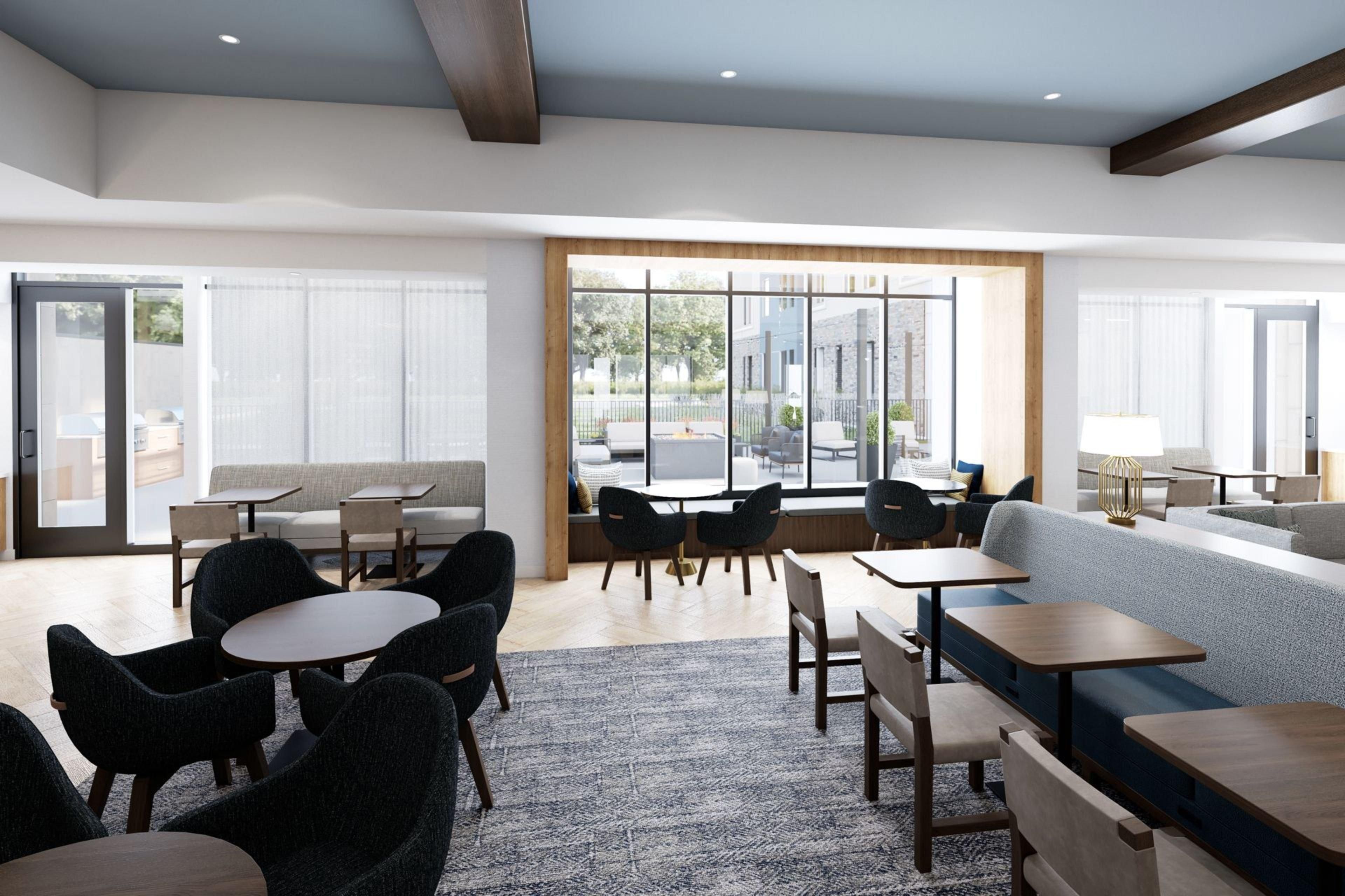 Un hall d’hôtel moderne, doté d’espaces aménagés avec des sièges, des tables et de grandes fenêtres offrant une vue sur l’extérieur.