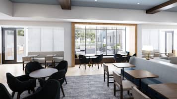 Un moderno vestíbulo de hotel con zonas de estar, mesas y grandes ventanales que ofrecen vistas al exterior.