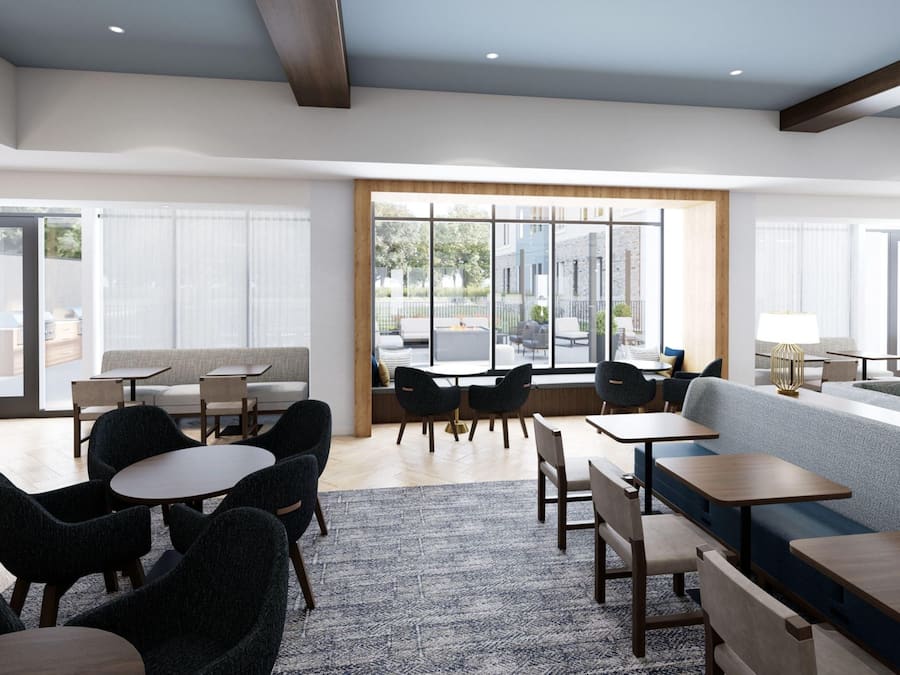 A modern hotel lobby with seating areas, tables, and large windows offering views of the outdoors.