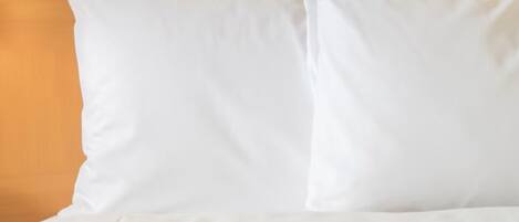 A bed with white bedding and pillows against a brown headboard.