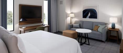 A hotel room with a large bed, a desk with a flat-screen TV, a gray sofa, a small round table, and a lamp.